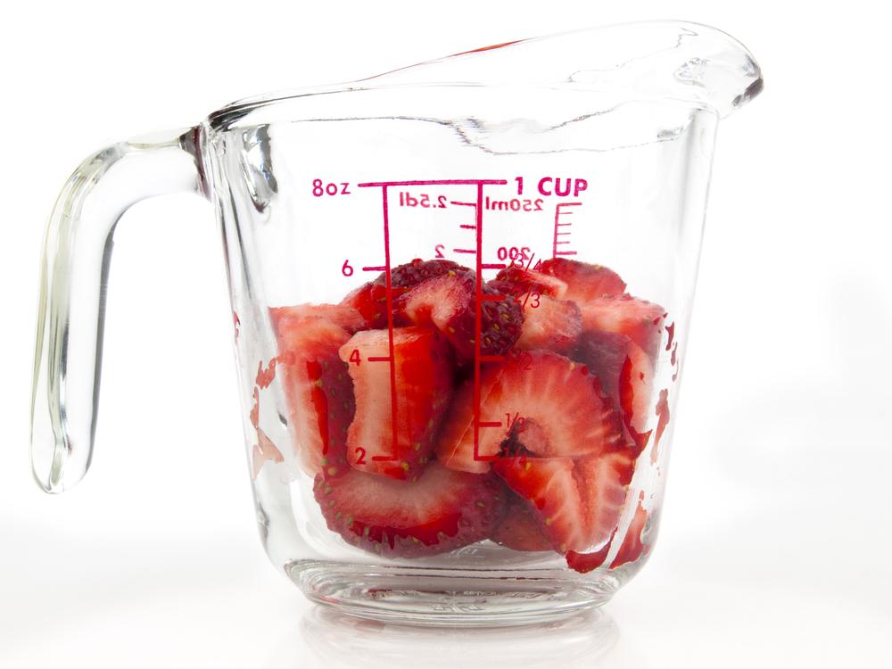 Glass measuring cup filled with sliced strawberries.